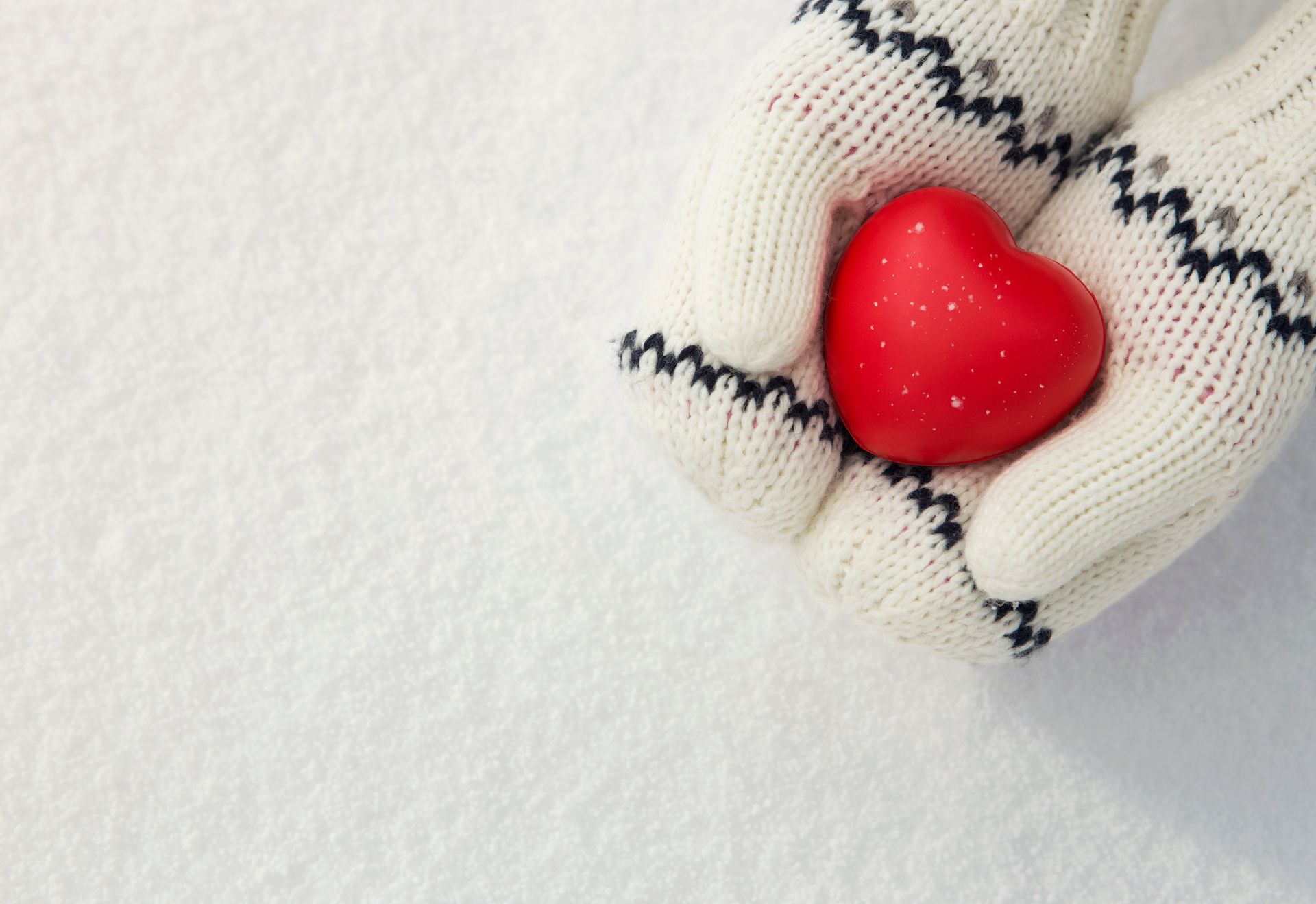 Kids hands with mittens holding a red heart as a gift